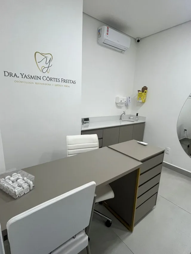 Sala com mesa e o letreiro Dra. Yasmin Côrtes Freitas, Odontologia restauradora e estética dental, na parede