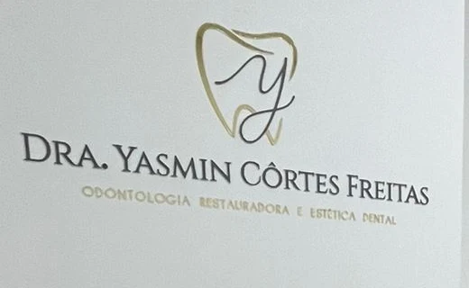 Letreiro com o símbolo de dente e a letra Y, o nome Dra. Yasmin Côrtes Freitas e a frase Odontologia restauradora e estética dental